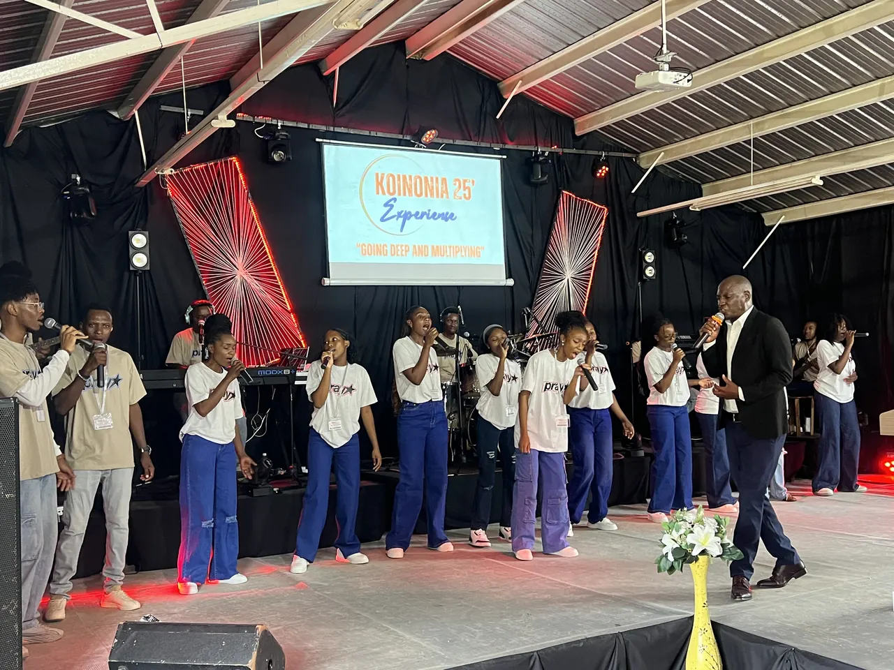 Singers lead praise beneath the Koinonia 25 Experience screen, Going Deep and Multiplying