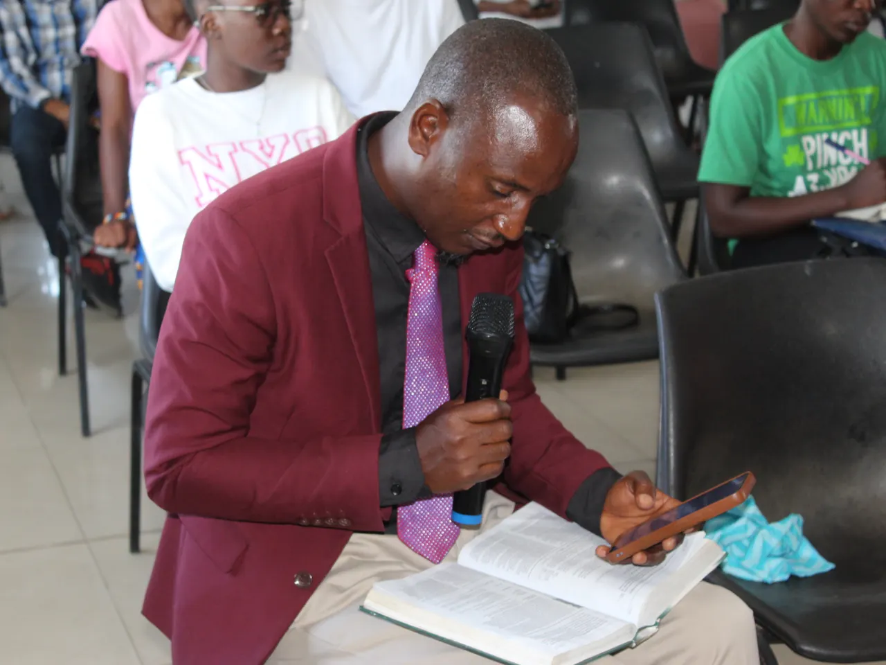 A man reads aloud from his open Bible, microphone in hand, during Sunday Bible study